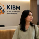 Seorang pasien sedang berada di area penerimaan KIBM dengan latar belakang logo dan identitas Klinik Intervensi Biologi Medis, menggambarkan pendekatan Gut, Immune & Inflammation Health dalam memahami hubungan kesehatan usus, sistem imun, dan inflamasi kronis.